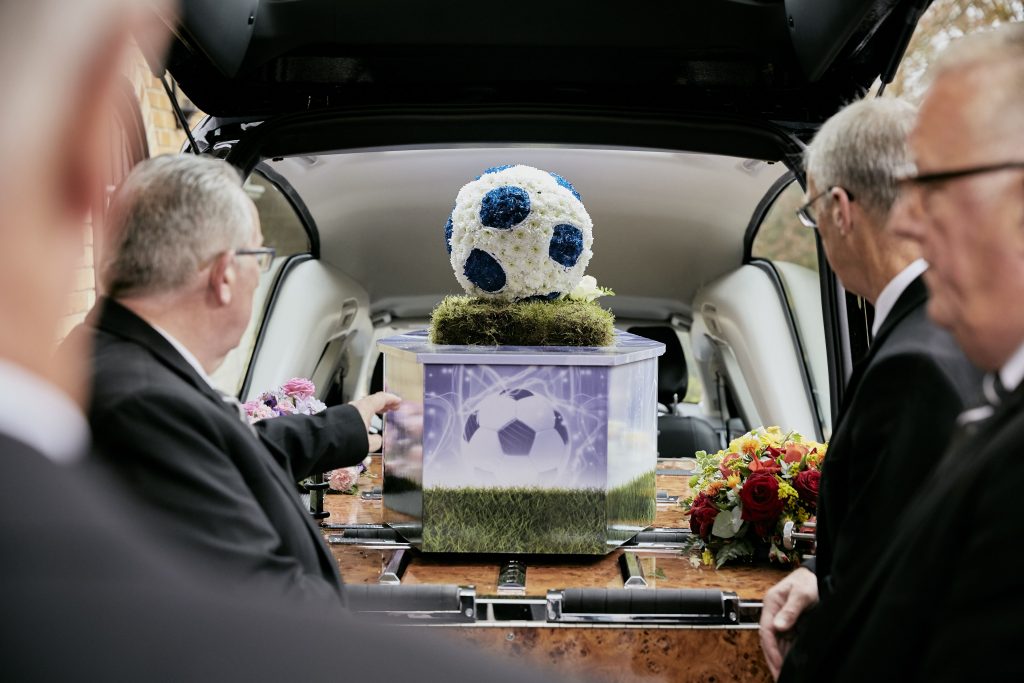 A coffin decorated with a football and a floral arrangement in the shape of a football