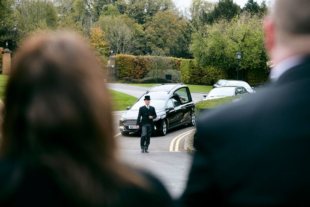 A funeral procession led by a black hearse